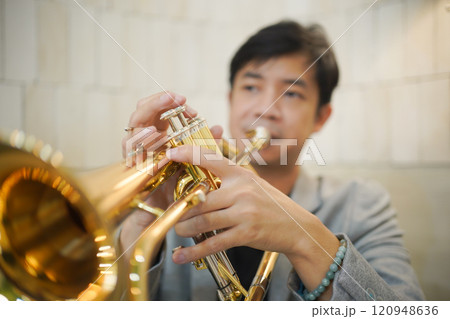 Asian man plays cornet. A solo Asian skillful musician is playing or practicing cornet in the restaurant. A man enjoy playing cornet or trumpet. Asian man plays cornet. A solo Asian skillful musician is playing or practicing cornet in the restaurant. A man enjoy playing cornet or trumpet. 120948636