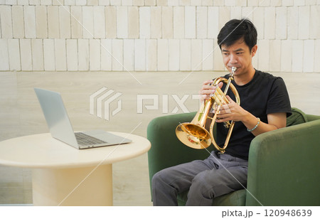 Asian man plays cornet. A solo Asian skillful musician is playing or practicing cornet in the restaurant. A man enjoy playing cornet or trumpet. 120948639