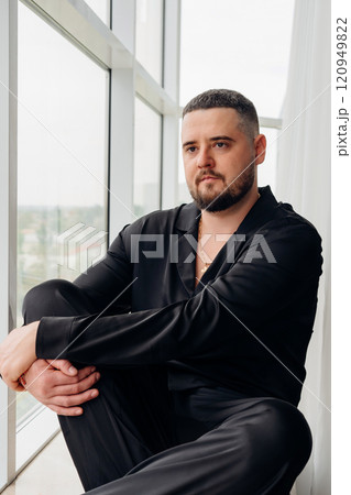 A man in black silk pajamas is sitting on the windowsill. A man in black silk pajamas is sitting on the windowsill. 120949822