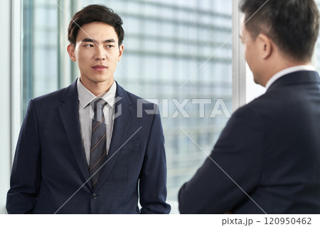 two asian businessmen chatting in office two asian businessmen chatting in office 120950462