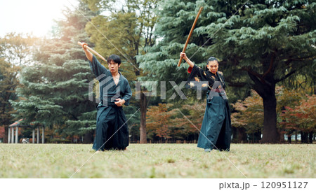 Sword, martial arts and people in outdoor training together for aikido, fight coaching or samurai challenge in nature. Warrior, Japanese man and woman in park for traditional bokken battle with wood Sword, martial arts and people in outdoor training together for aikido, fight coaching or samurai challenge in nature. Warrior, Japanese man and woman in park for traditional bokken battle with wood 120951127