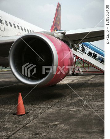 A close-up of an airplane engine on the tarmac, with a small orange cone in the foreground. 120951409