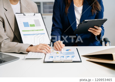 Business documents on office table with smart phone and laptop and two colleagues discussing data in the background Business documents on office table with smart phone and laptop and two colleagues discussing data in the background 120953465
