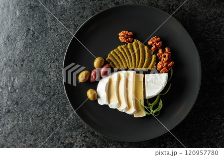 Camembert cream cheese with olives, rosemary, and walnuts on a black plate. 120957780
