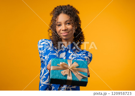 Happy teenager girl gift box on yellow background. Young lady smiling, gives you 120958723