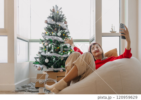 Happy red shirt woman making a video call holiday greeting with her friends and family showing the Christmas tree. Happy red shirt woman making a video call holiday greeting with her friends and family showing the Christmas tree. 120959629