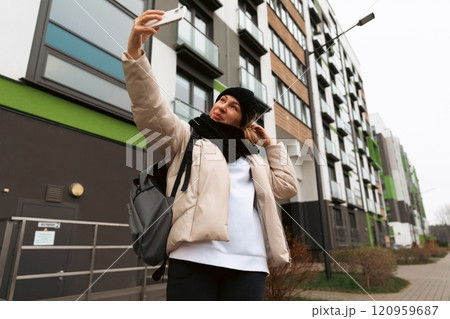 Person taking a selfie in front of a modern building on a cloudy day in an urban area 120959687