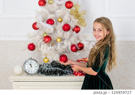 Girl celebrate christmas. Child put christmas ornament ball on artificial white tree. Top christmas decorating ideas for kids room. Kids can brighten up christmas tree by creating their own ornaments Girl celebrate christmas. Child put christmas ornament ball on artificial white tree. Top christmas decorating ideas for kids room. Kids can brighten up christmas tree by creating their own ornaments 120959727