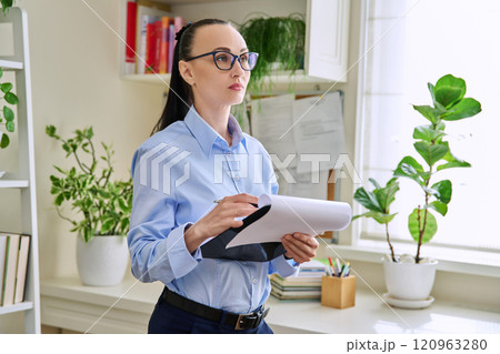 Portrait of serious female psychotherapist with clipboard at workplace in office Portrait of serious female psychotherapist with clipboard at workplace in office 120963280