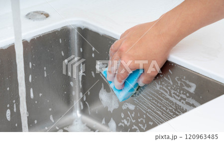 Scrubbing a kitchen sink with soapy water using a sponge under running water. 120963485