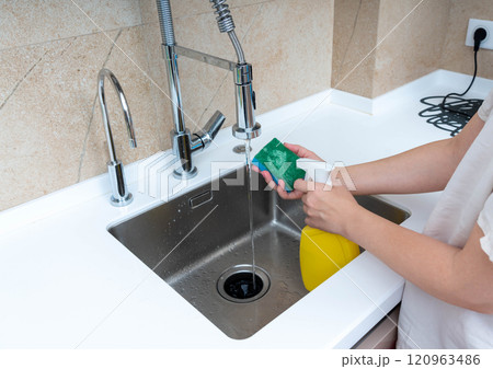 Washing dishes with a sponge and soap under running water in a modern kitchen sink. 120963486