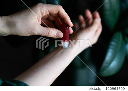 Aromatherapy. Woman with roller bottle applying essential oil onto wrist against light green background, closeup Aromatherapy. Woman with roller bottle applying essential oil onto wrist against light green background, closeup 120965890