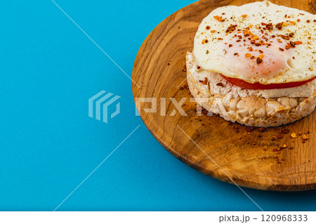 Egg on rice bread with tomato and cheese on a wooden plate on a blue background Egg on rice bread with tomato and cheese on a wooden plate on a blue background 120968333