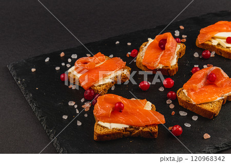 Toasts with butter, mozzarella and salmon on a stone board on a black background Toasts with butter, mozzarella and salmon on a stone board on a black background 120968342