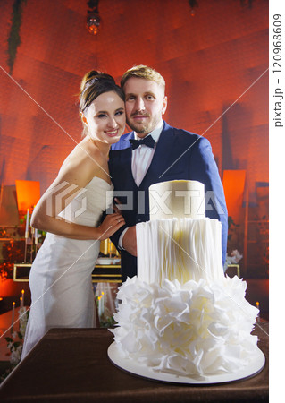 The bride and groom stand next to a wedding cake. 120968609