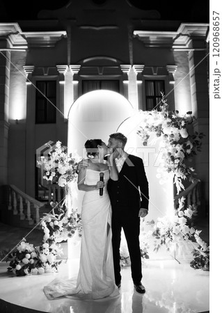 a bride and groom in front of a wedding arch decorated with flowers a bride and groom in front of a wedding arch decorated with flowers 120968657
