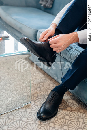 without a face. A man in blue pants ties his shoelaces on black shoes.  120968663