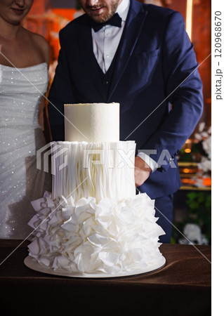 The bride and groom stand next to a wedding cake. 120968670