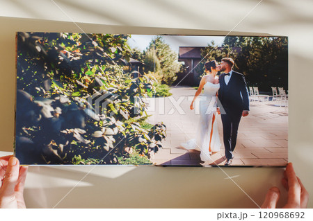Female hands flipping through a photo book with wedding photos on a white table 120968692