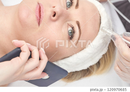 Mature caucasian female receiving cosmetic treatment while on phone in clinic 120970685