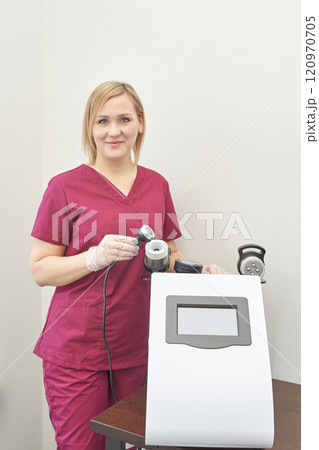 Female caucasian adult in burgundy scrubs operating medical equipment in clinic 120970705