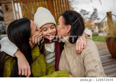 Mature daughter, grandmother and granddaugter sitting on wooden patio, hugging. Mother's day and multigenerational family concept. Mature daughter, grandmother and granddaugter sitting on wooden patio, hugging. Mother's day and multigenerational family concept. 120972034