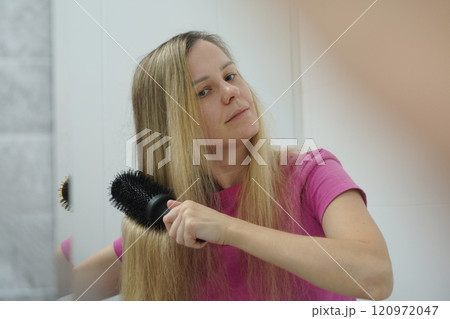 A woman is expertly styling her hair using a blow dryer and brush while in the bathroom 120972047