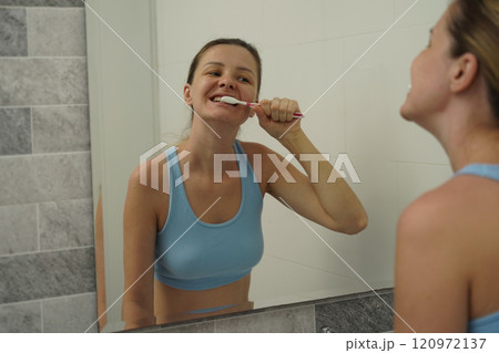 Young woman in a modern bathroom washing her face and brushing her teeth  120972137