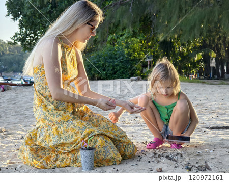 A mother and her daughter as they collect shells together  120972161