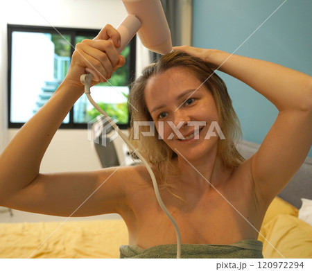 A woman is expertly styling her hair using a blow dryer and brush while in the bathroom A woman is expertly styling her hair using a blow dryer and brush while in the bathroom 120972294