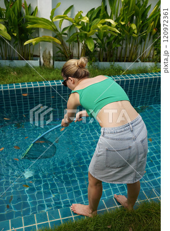A young woman clean leaves out of a pool  120972361