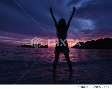 A woman in silhouette poses at sunset surrounded by tranquil ocean A woman in silhouette poses at sunset surrounded by tranquil ocean 120972465