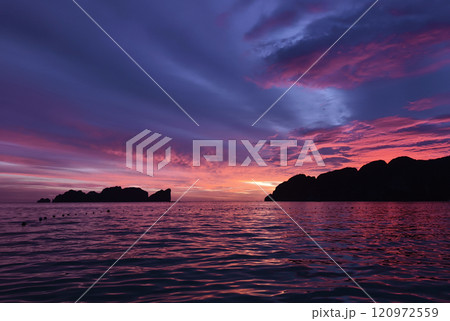 A stunning sunset is casting vibrant hues of color over a tranquil ocean 120972559