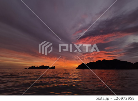 A stunning sunset is casting vibrant hues of color over a tranquil ocean 120972959