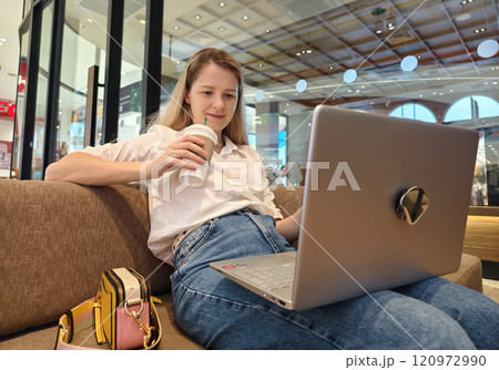 A young woman enjoys coffee while working on her laptop A young woman enjoys coffee while working on her laptop 120972990