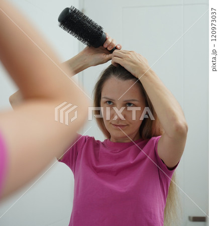 A woman is expertly styling her hair using a blow dryer and brush while in the bathroom 120973037