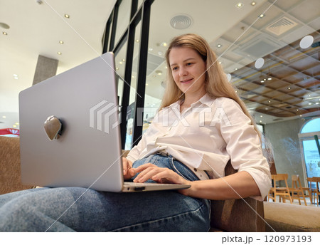 A young woman enjoys coffee while working on her laptop A young woman enjoys coffee while working on her laptop 120973193