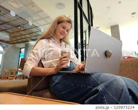 A young woman enjoys coffee while working on her laptop  120973224