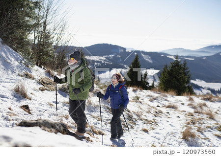 Active seniors walking through snowy winter nature. Romantic winter hike for an elderly couple in snowy mountains. 120973560