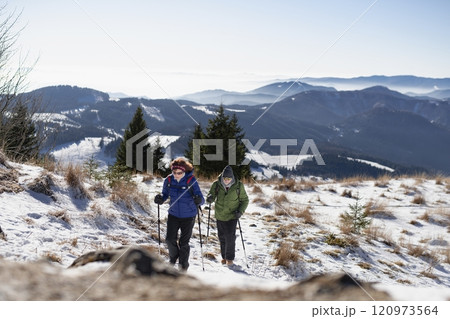 Active seniors walking through snowy winter nature. Romantic winter hike for an elderly couple in snowy mountains. 120973564