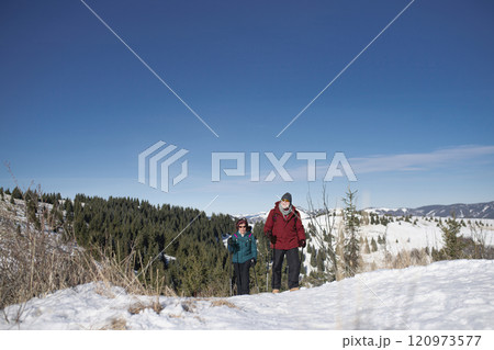 Active seniors walking through snowy winter nature. Romantic winter hike for an elderly couple in snowy mountains. 120973577