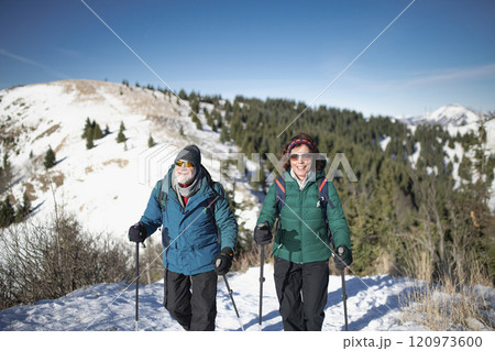 Active seniors walking through snowy winter nature. Romantic winter hike for an elderly couple in snowy mountains. 120973600