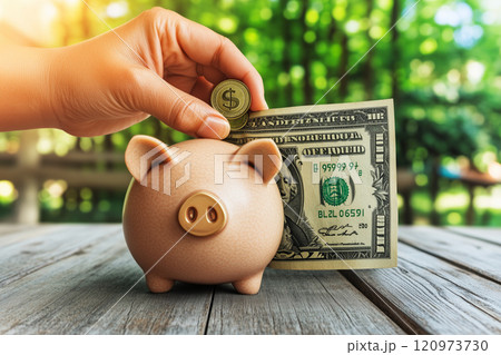 Hand Inserting Coin and Dollar Bill into Piggy Bank with Blurred Green Background, Representing Savings, Investment, and Personal Wealth Management Concepts Hand Inserting Coin and Dollar Bill into Piggy Bank with Blurred Green Background, Representing Savings, Investment, and Personal Wealth Management Concepts 120973730