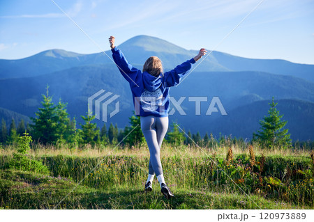 Woman tourist on grassy hill with beautiful mountain landscape with Hoverla in background. Young female wearing blue hoodie and grey leggings. 120973889