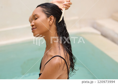 Relaxed Woman Enjoying Spa Day While Brushing Long Wet Hair by Poolside 120973994