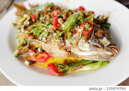 Deep fried sea bass topped with fresh bird eye chilli and vegetable ingredient on white dish 120974764