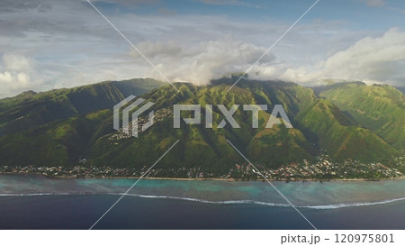 Zoom in panoramic flight to Tahiti island in south pacific ocean. Green mountains hills peaks under cloudy sky, turquoise water, vibrant coral reef and coastal village. Remote paradise, exotic travel 120975801