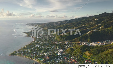 Stunning aerial view panorama of Punaauia city nestled between lush green mountains hills canyon and turquoise pacific ocean lagoon. Tahiti tropical island in sunset glow. Explore French Polynesia 120975805