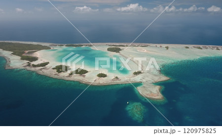 Aerial view of Rangiroa, largest atoll in Tuamotus archipelago, French Polynesia, showcasing vibrant turquoise lagoon, coral reefs, and lush vegetation under a cloudy sky. Remote wild nature paradise 120975825