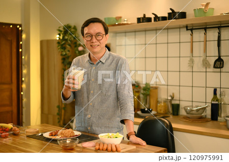 Smiling senior man holding a glass of milk and enjoying breakfast in his home kitchen Smiling senior man holding a glass of milk and enjoying breakfast in his home kitchen 120975991